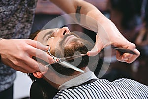 Hairdresser doing haircut of beard to young attractive man