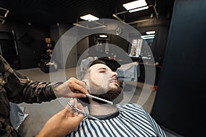 Hairdresser doing haircut of beard using comb and scissors