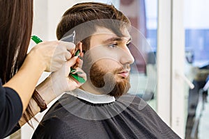 Hairdresser doing haircut for male client, man with beard using professional hairdresser tools, equipment on hairdresser work