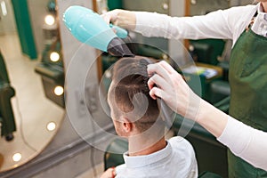 Hairdresser dries hair of stylish man. Young handsome guy doing hair styling at a hairdresser