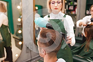 Hairdresser dries hair of stylish man. Young handsome guy doing hair styling at a hairdresser