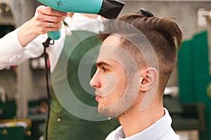 Hairdresser dries hair of stylish man. Young handsome guy doing hair styling at a hairdresser