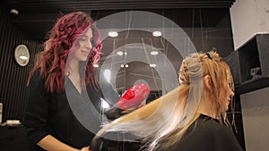 A hairdresser dries long blond hair with a hairdryer and a round brush in a hair salon.