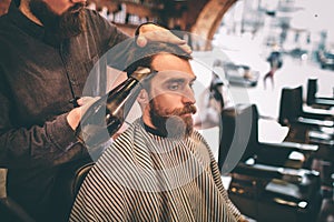 Hairdresser is drying the customer`s hair with a tair dryer. The customer is looking down.