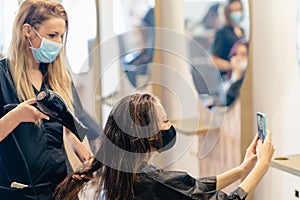 Hairdresser drying her client`s hair with a hairdryer wearing protective masks in a beauty centre.