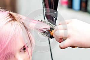 Hairdresser is drying pink hair with hair dryer and round brush
