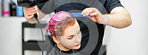 A hairdresser is drying the pink hair of the young woman in a beauty salon.