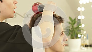 Hairdresser drying and styling male hair after cutting in hairdressing salon. Close up barber styling hair with dryer