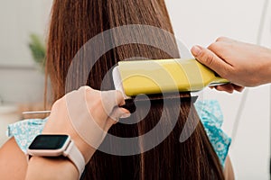 Hairdresser evens out the client& x27;s brown hair with a curler