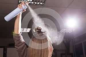 Hairdresser fixing a topknot of a model with a hair spray