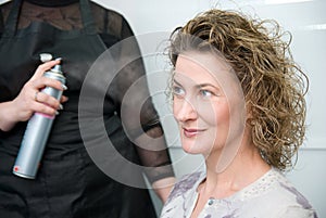 Hairdresser fixing woman hair with hairspray photo