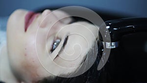 Hairdresser in gloves washing brunette girl hair over sink in beauty shop.