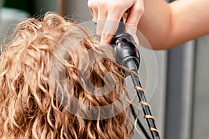 Hairdresser hands curl woman`s hair by curling iron