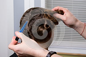 The hairdresser holds a hair clip in his hand and makes a hairdo for the child