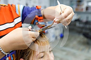 A hairdresser holds a pair of scissors and a comb. Woman getting a new haircut. Beauty treatments and hair care concept