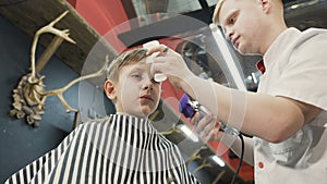 The hairdresser make a stylish haircut for a little boy in barbershop. Barber doing cutting hair with hair trimmer and