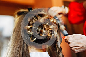 Hairdresser makes bride a high wedding styling with curls with a curling iron. Close-up