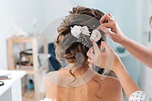 Hairdresser makes an elegant hairstyle styling bride with white flowers in her hair
