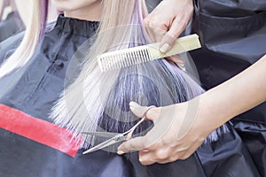 Hairdresser makes haircut to a girl in with long blonde hair. Hairdresser hands holding scissors