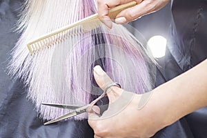 Hairdresser makes haircut to a girl in with long blonde hair. Hairdresser hands holding scissors