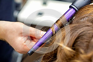 Hairdresser makes hairstyle by curling iron