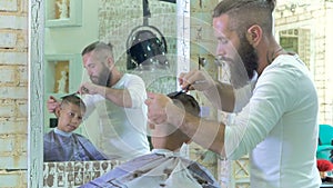 Hairdresser makes a hairstyle for little boy in barber shop