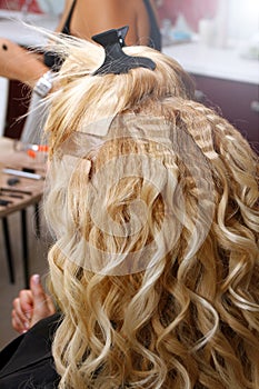 Hairdresser and makeup stylist are making hairstyle and makeup of the bride in the beauty salon. Hairstylist curls hair of Blond g