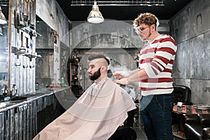 Hairdresser man shaves a client with a beard in a barbershop