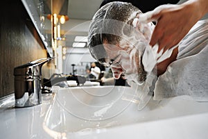 Hairdresser man washes client head in barbershop, close up