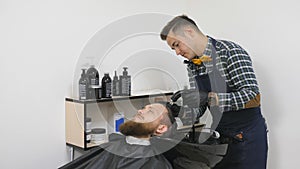 Hairdresser for men. Barbershop. Caring for the beard. Barber with hair clipper works on hairstyle for bearded guy