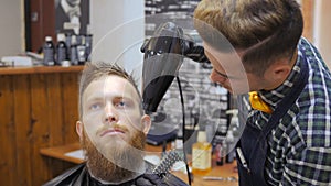 Hairdresser for men. Barbershop. Caring for the beard. Barber with hair clipper works on hairstyle for bearded guy