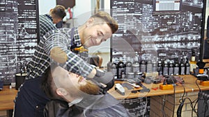 Hairdresser for men. Barbershop. Caring for the beard. Barber with hair clipper works on hairstyle for bearded guy