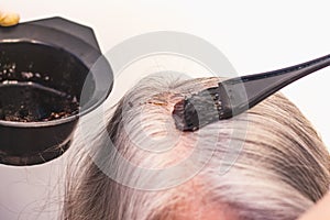 Hairdresser paints gray hair in dark color, apply the paint to the hair in the beauty salon