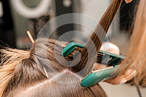 The hairdresser prepares a woman, makes a hairstyle with curls using a curling iron. Long light brown natural hair. Self