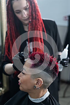 The hairdresser removes excess dye from the skin of a female with a cotton pad.Asian woman with a short haircut in a