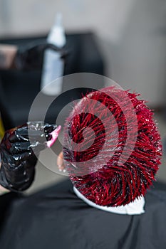 The hairdresser removes excess dye from the skin of a female with a cotton pad.Asian woman with a short haircut in a