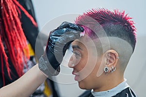 The hairdresser removes excess dye from the skin of a female with a cotton pad.Asian woman with a short haircut in a