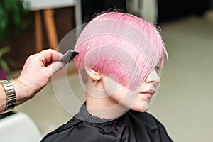 Hairdresser`s hand is combing pink hairstyle