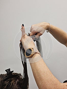 Hairdresser's hands cut long brown hair. Modeling brown hair by scissors and comb of young brunette woman.