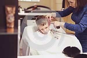 Hairdresser`s hands making hairstyle to little boy, close up