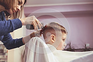 Hairdresser`s hands making hairstyle to little boy, close up