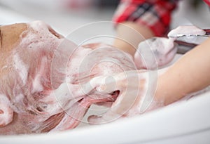 hairdresser`s hands washing the client`s pink hair with foam shampoo