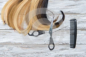 Hairdresser`s scissors with comb and strand of hair on wooden background. Hairdresser service