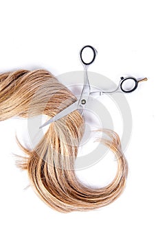 Hairdresser's scissors with strand of blond hair on white background