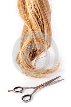 Hairdresser's scissors with strand of blond hair on white background