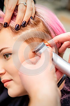 Hairdresser shaves female temple with pink hair by electric shaver in a hairdresser salon, close up.