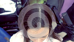 Hairdresser straights dark brown hair of beautiful woman using hair tongs in beauty salon.