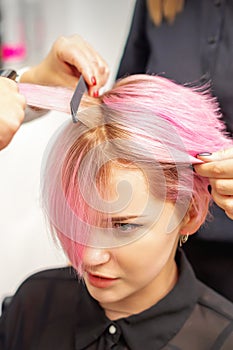 Hairdresser straights pink hair of woman by hair iron