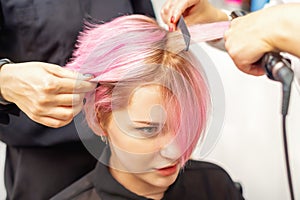 Hairdresser straights pink hair of woman by hair iron