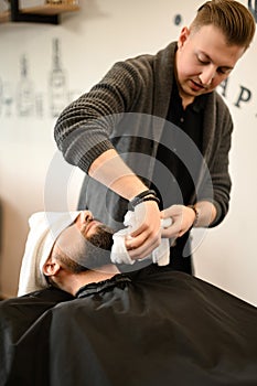 Hairdresser stylist wipes the remains of shaving gel with towel after shaving the beard